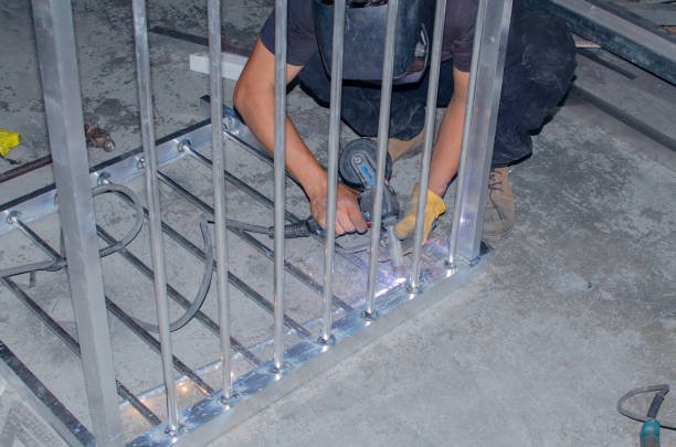 A man skillfully welding metal bars for garage door repair, sparks flying, showcasing precision and craftsmanship in a workshop setting.