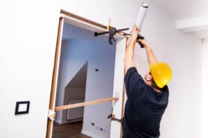 A man wearing a hard hat prepares to begin door frame repair for water damage on a home construction site.