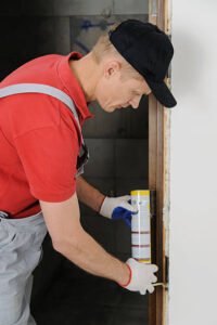 A man in a red shirt and white gloves performing door frame repair for water damage, focused on restoring structural integrity.