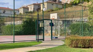 A residential basketball court enclosed by a chain link fence with a gate, highlighting chain link fence gate installation in a neighborhood setting.