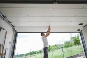 A man performs emergency garage door repair inside a garage, using tools and materials to restore door function.