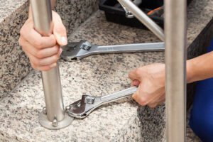 Individual fixing a metal railing with wrenches, focusing on stair handrails.